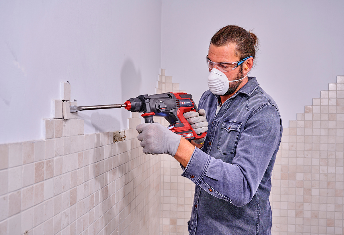 Απεικονίζεται άντρας να χρησιμοποιεί το πιστολέτο για εργασία σε πλακίδια στον τοίχο.